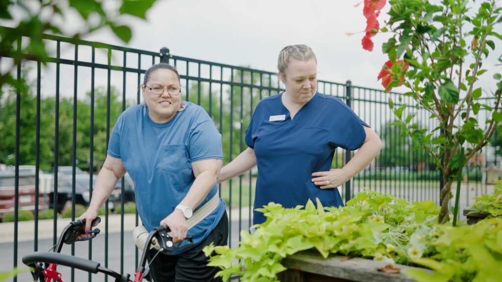 A woman and a nurse walk around a garden at a short term care facility