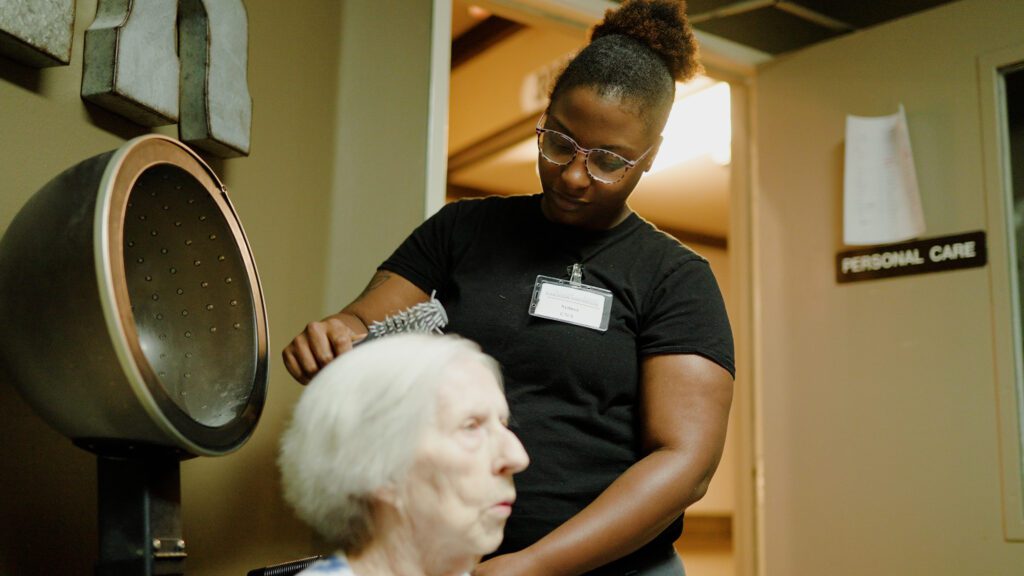 A stylist working on a woman's hair at a skilled nursing facility
